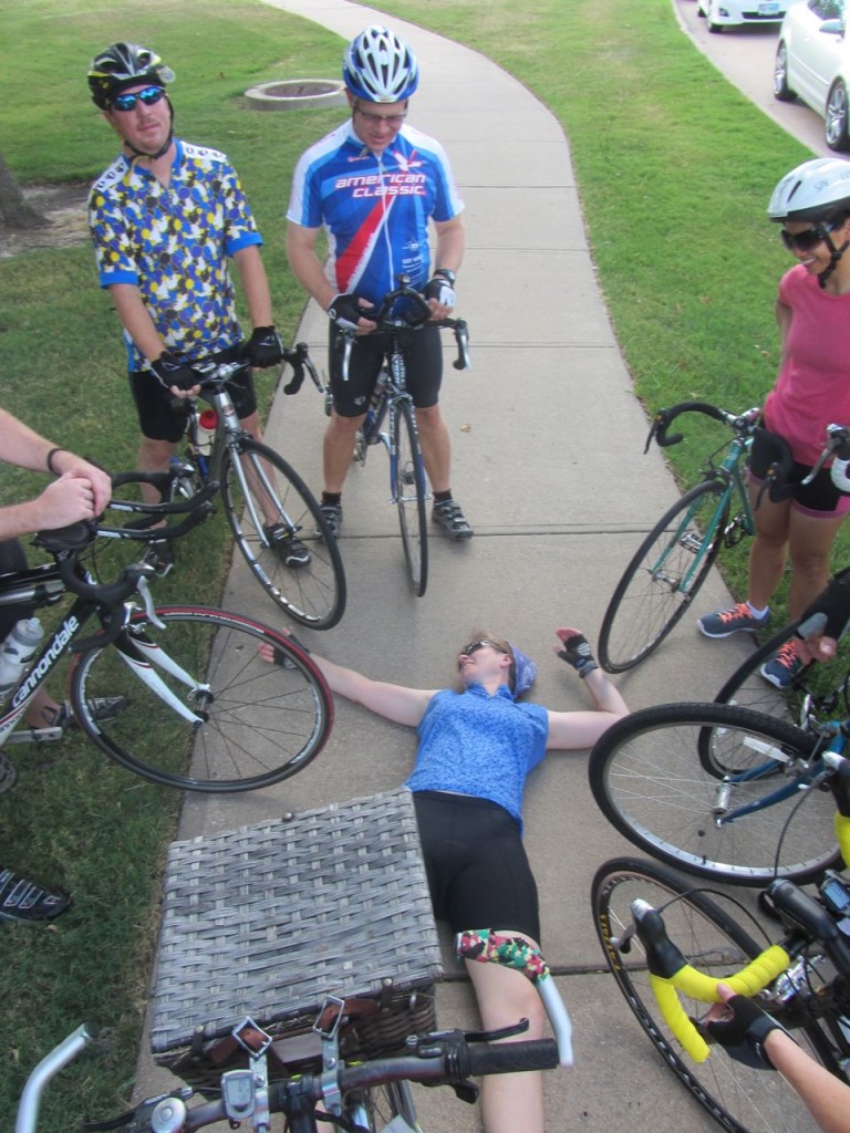 Cyclists surrounding Jean Marie who is spread out on the ground.